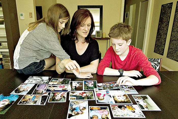 Băieţelul, alături de sora şi de mama lui, se uită la pozele din copilărie