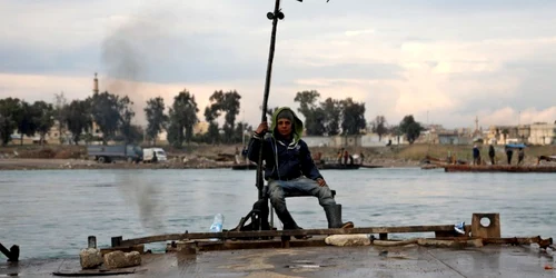 Un tânăr stă pe barca pe care o foloseşte pentru a transporta maşini şi persoane de pe cele două maluri ale râului Eufrat în centrul oraşului Raqqa în nord-estul Siriei FOTO EPA-EFE / Ahmed Mardnali