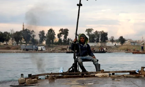 Un tânăr stă pe barca pe care o foloseşte pentru a transporta maşini şi persoane de pe cele două maluri ale râului Eufrat în centrul oraşului Raqqa în nord-estul Siriei FOTO EPA-EFE / Ahmed Mardnali