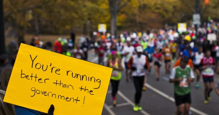 Alergatori trec prin Manhattan in timpul maratonului dela New York pe margine cineva tine un afis care taxeaza politica guvernului foto reuters