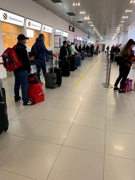 Oamenii stau la coadă la check-in păstrând diatanța între ei