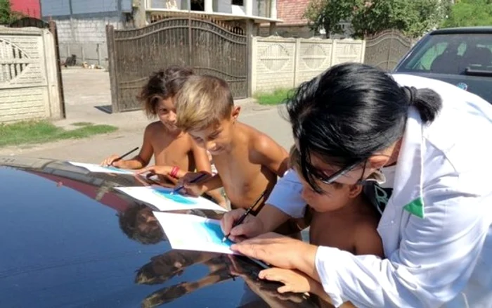 
    Asistentul medical comunitar  lucrează fișe cu copiii  pe capota mașinii    