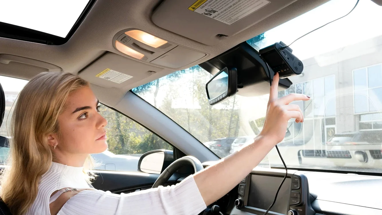 Șoferiță reglează o cameră auto duală cu imaginea camerei spate vizibilă în oglindă