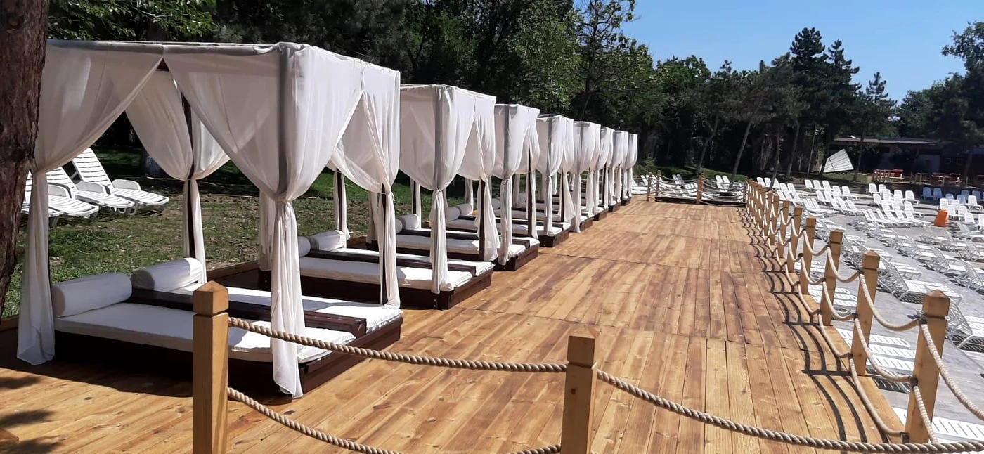 Baldachine așezate pe o podea de lemn, după zona în care sunt șezlongurile puse pe nisip