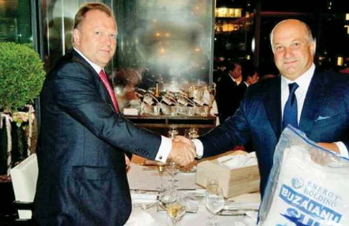 Bogdan Buzăianu (dreapta)  cu o mână salutându-l pe Marius Vizer, iar cu cealaltă strângând  o pungă „Energy Holding“,  în 2010, la Tokyo   