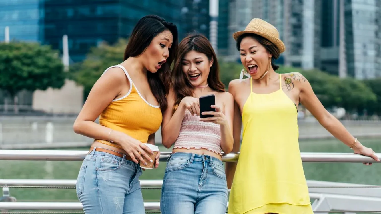 Trei tinere din China râd privind ofertele de Singles Day de pe telefon