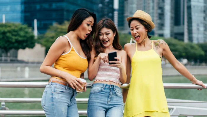 Trei tinere din China râd privind ofertele de Singles Day de pe telefon