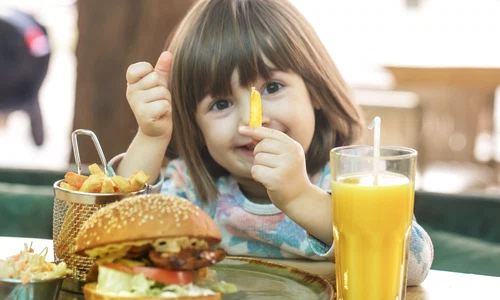 little cute girl eating fast food sandwich with fries orange juice cafe fast food concept jpg