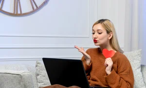 virtual love cute young blonde girl cozy sweater computer distance date holding paper heart jpg