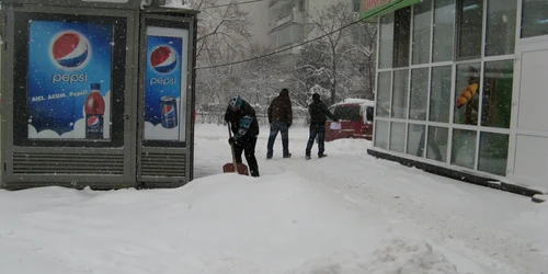 O vânzătoare curăţă de zor zăpada în faţa unui chioşc de ziare din Iaşi