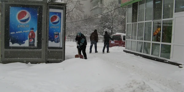 O vânzătoare curăţă de zor zăpada în faţa unui chioşc de ziare din Iaşi