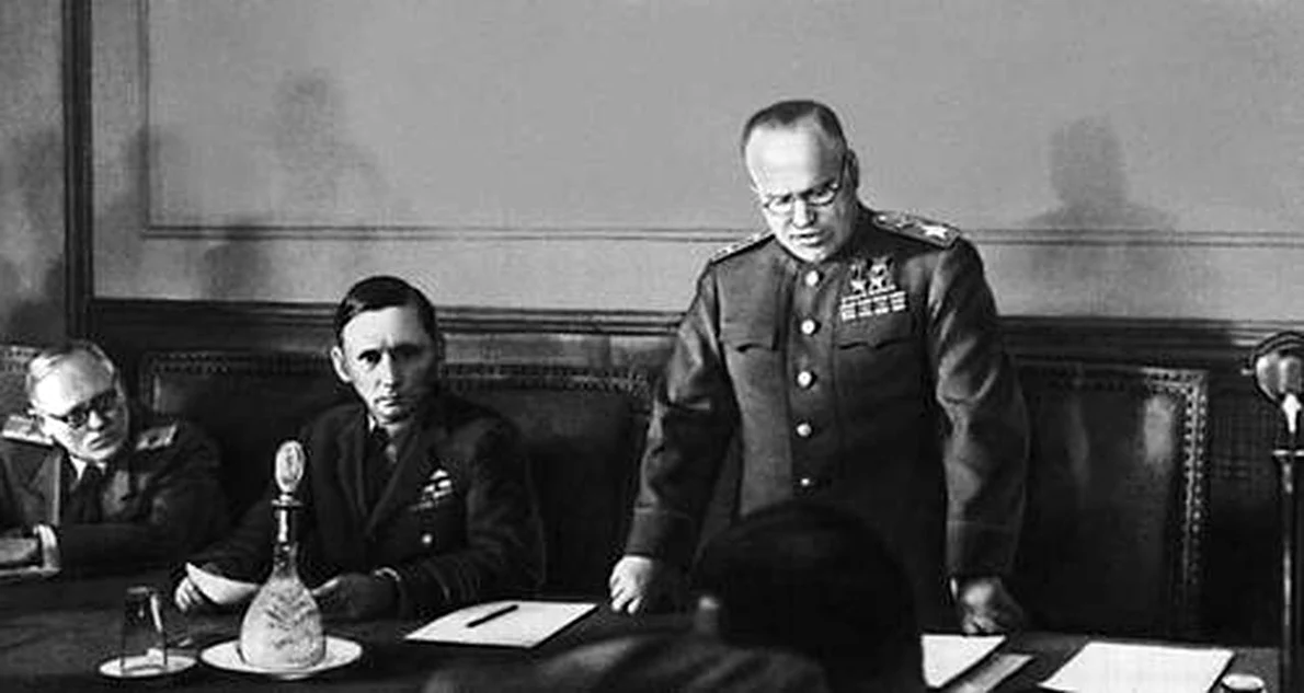 Mareşalul sovietic Gheorghi Jukov citește actul capitulării Germaniei la Cartierul său General din Berlin. La dreapta sa se află Mareşalul Forţelor Aeriene al Regatului Unit, Arthur Tedder (© Wikimedia Commons)