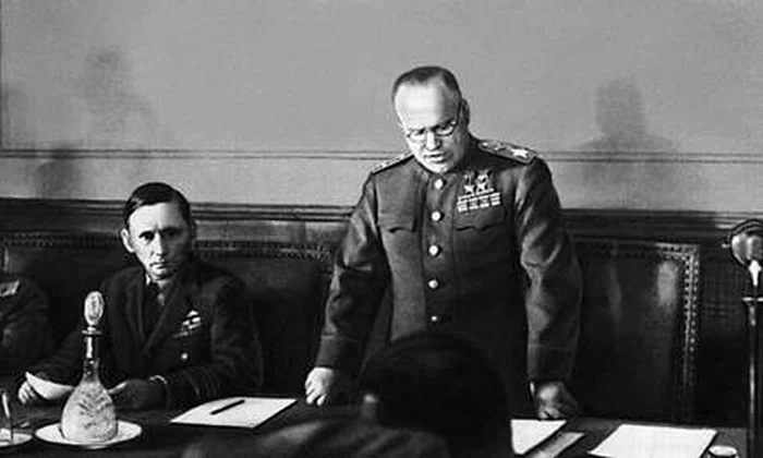 Mareşalul sovietic Gheorghi Jukov citește actul capitulării Germaniei la Cartierul său General din Berlin. La dreapta sa se află Mareşalul Forţelor Aeriene al Regatului Unit, Arthur Tedder (© Wikimedia Commons)