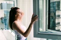 young woman opens plastic window fresh air smiling home jpg