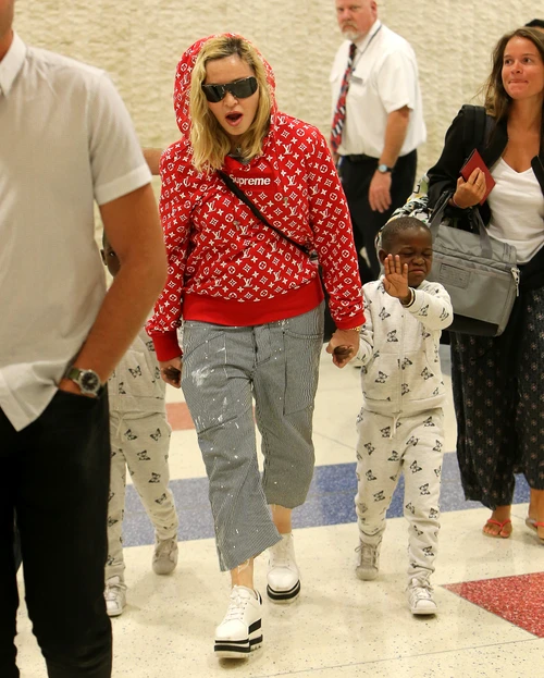 Madonna rocks a red supreme louis vuitton hoodie while touching down at JFK airport in New York holding her twins hands Estere and Stelle while Lourdes, David, and Mercy in tow after celebrating her 59th birthday in Italy jpeg