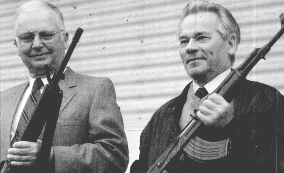 Americanul Eugene Stoner (stânga) și Mihail Kalașnikov țin în mâini puștile de asalt pe care le-au proiectat, AR-15 și AK-47, la 22 mai 1990