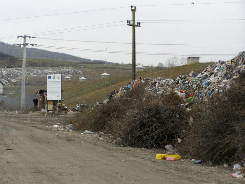 Lângă mormanele de gunoi stă mândră plăcuţa care ne spune că fosta groapă de gunoi a fost închisă cu fonduri europene FOTO: George Tudosa