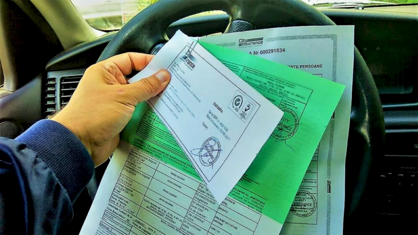 Un șofer ține polița de asigurare cu o mână, deasupra volanului