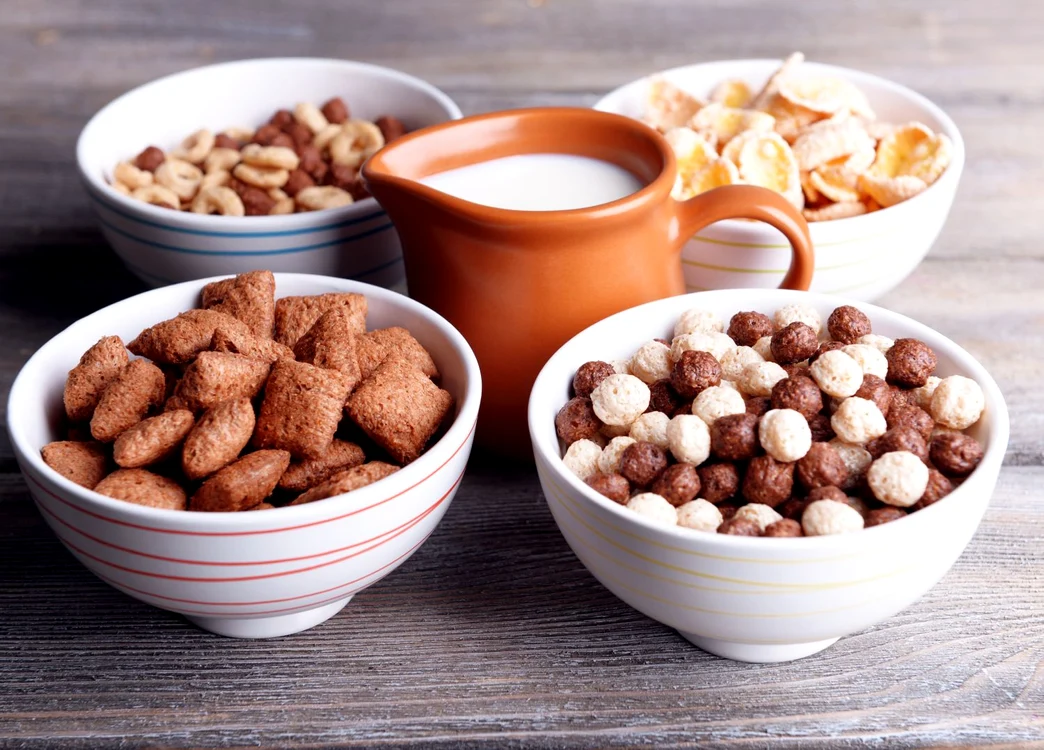 Various sweet cereals in ceramic bowls and jug with milk on color wooden background jpeg