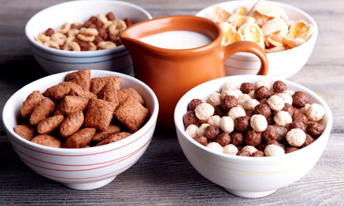 Various sweet cereals in ceramic bowls and jug with milk on color wooden background jpeg