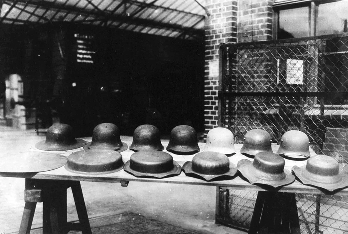 Între 1914 şi 1918,  când s-a sfârşit războiul,  peste 65 de milioane de soldaţi au fost mobilizaţi la scară mondială - iar asta a necesitat multe provizii şi harnaşament. În fotografie apare o masă dintr-o fabrică de căşti de oţel din Lubeck,  Germania. Sunt prezentate stagiile prin care trece o cască până ajunge să fie purtată.