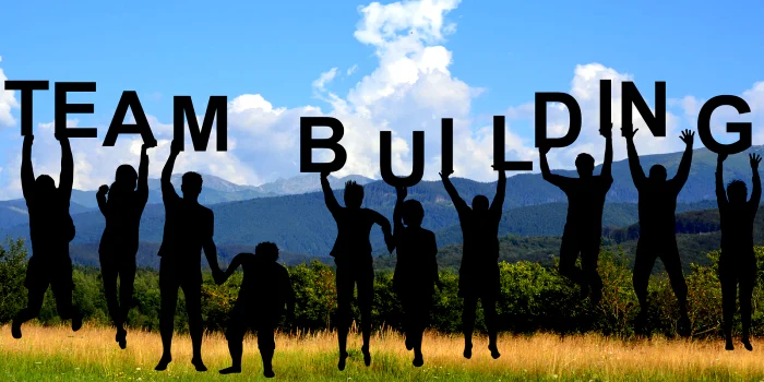 Angajați pe un câmp, ținând deasupra capului litere care formează cuvântul „Team Building”