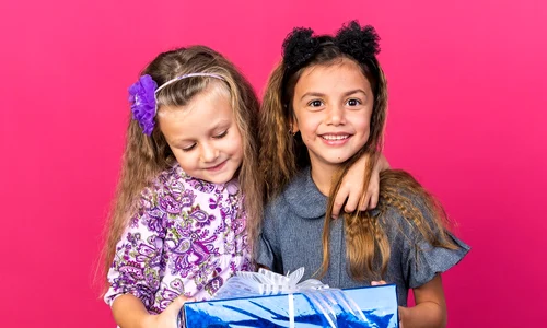 pleased little pretty girls holding gift box together isolated pink wall with copy space jpg