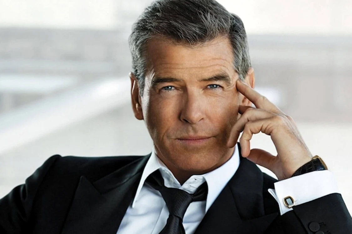 Pierce Brosnan, în costum, cu mâna la tâmplă