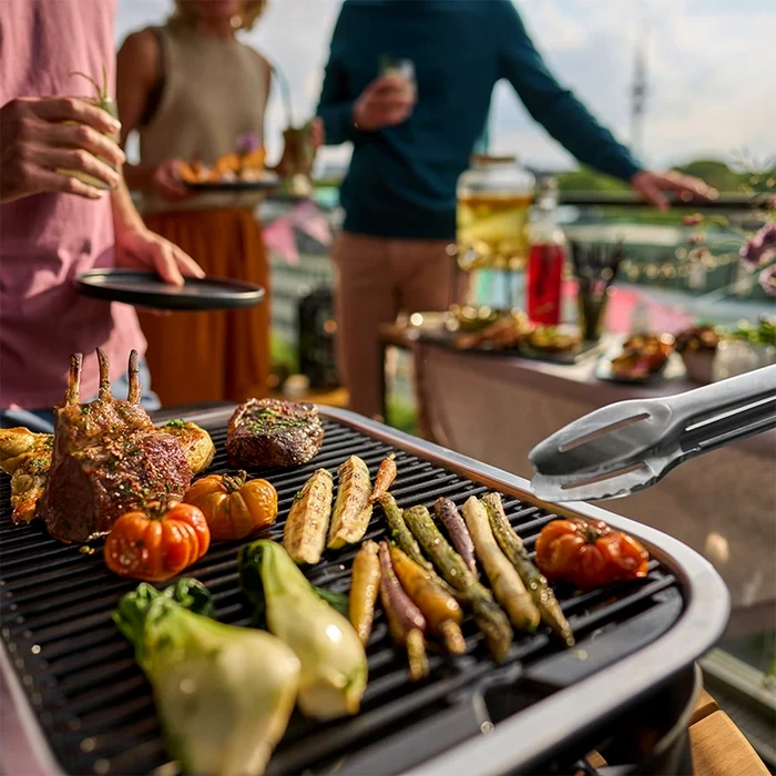 Grătar electric în mijlocul unei petreceri pe balcon prepară legume și carne Sursă Grill Expert