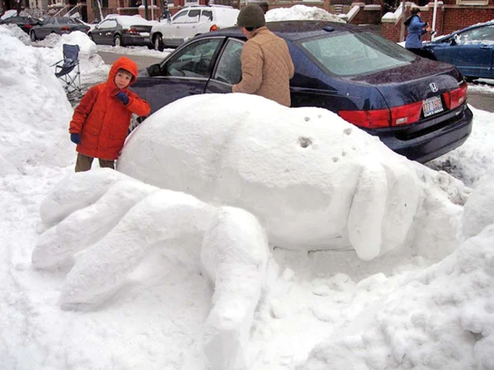 Un copil admiră pe stradă animalele modelate din omăt