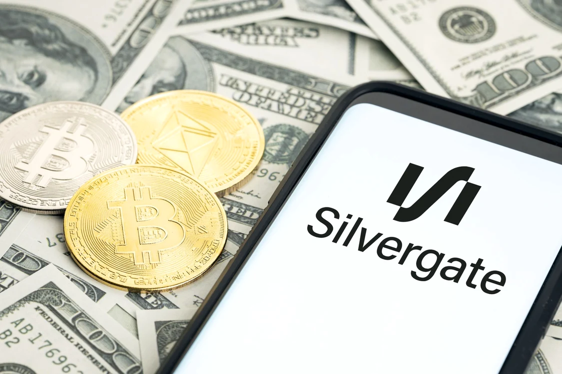 Telefon pe care este deschisă aplicația Silvergate așezat peste dolari și bitcoin