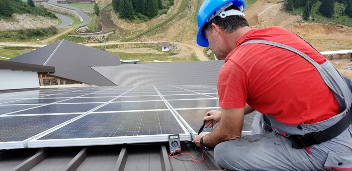Un instalator montează fotovoltaice pe un acoperiș