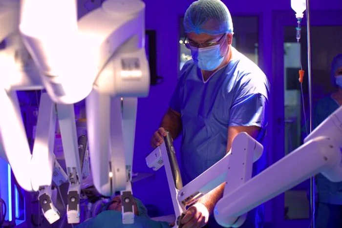 Medic coordonând un braț robotic în sala de operație