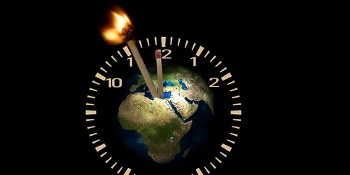 Globul pământesc în centrul unui ceas cu chibrituri drept pendule, unul dintre el fiind aprins   pixabay jpg