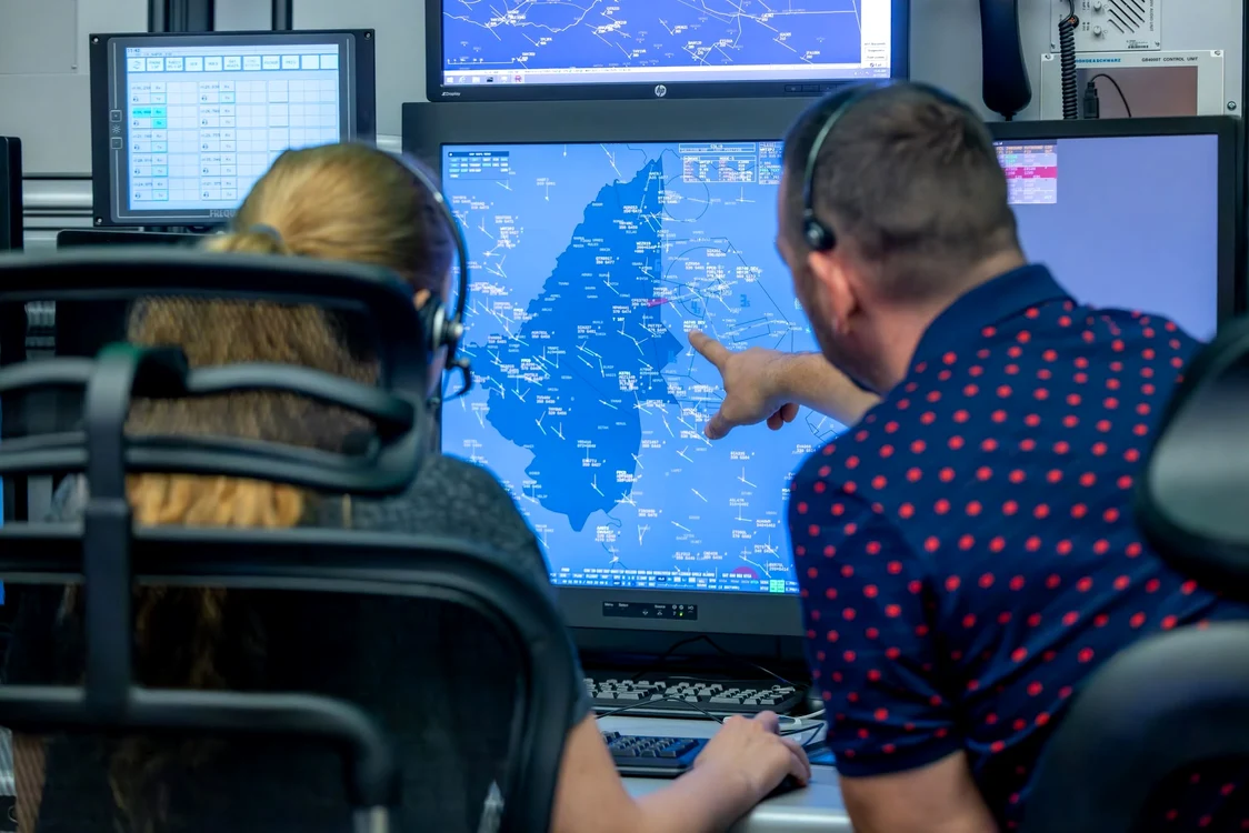 Doi controlori de trafic aerian analizează datele de zbor pe ecrane radar, în sala de control