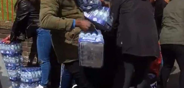 Mai multe persoane se îngrămădesc să apuce măcar câteva sticle cu apă, dacă nu un bax. Captură