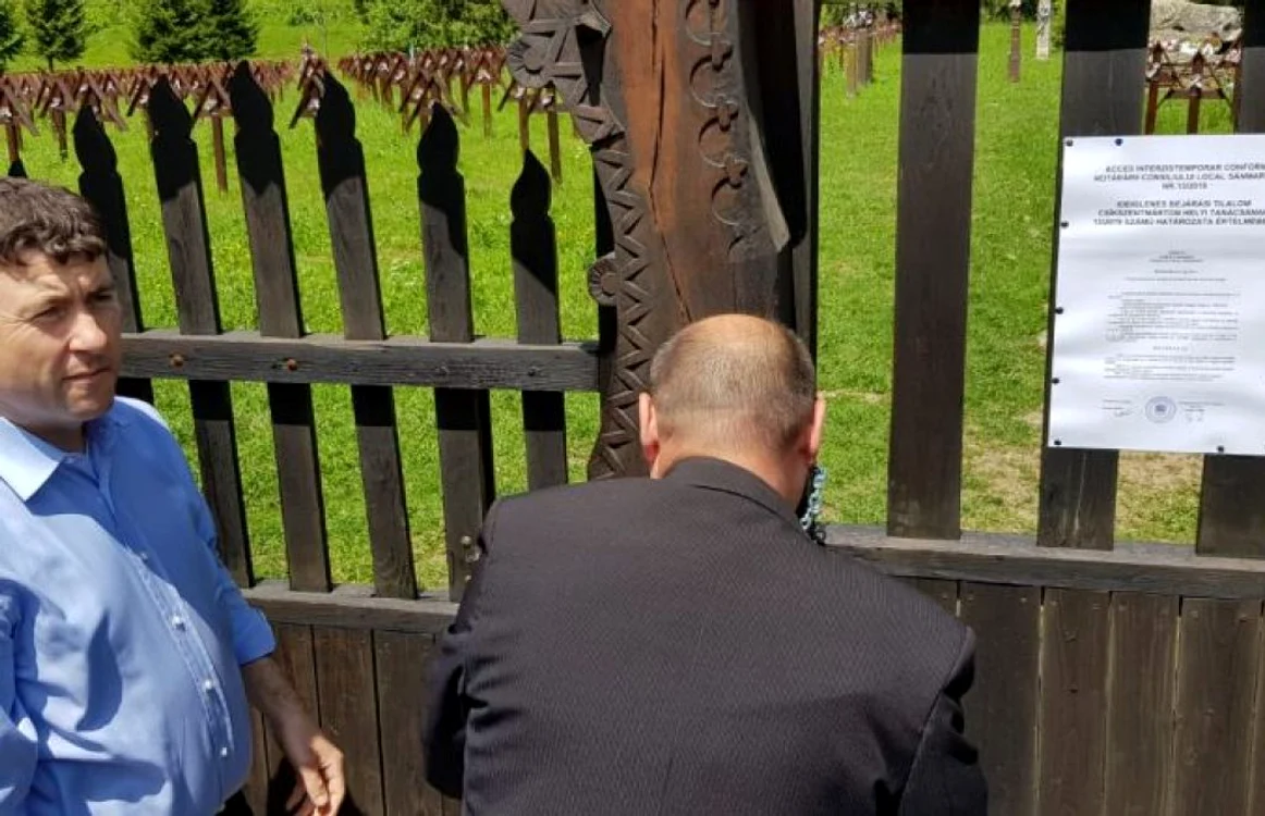 Preşedintele Consiliului Judeţean Harghita (stânga) încuie poarta de acces în Cimitirul Eroilor.