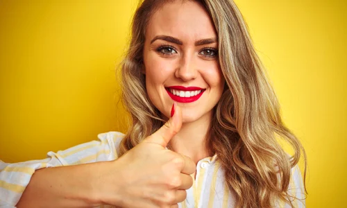 young beautiful woman wearing stripes shirt standing yellow isolated background happy with big smile doing ok sign thumb up with fingers excellent sign jpg
