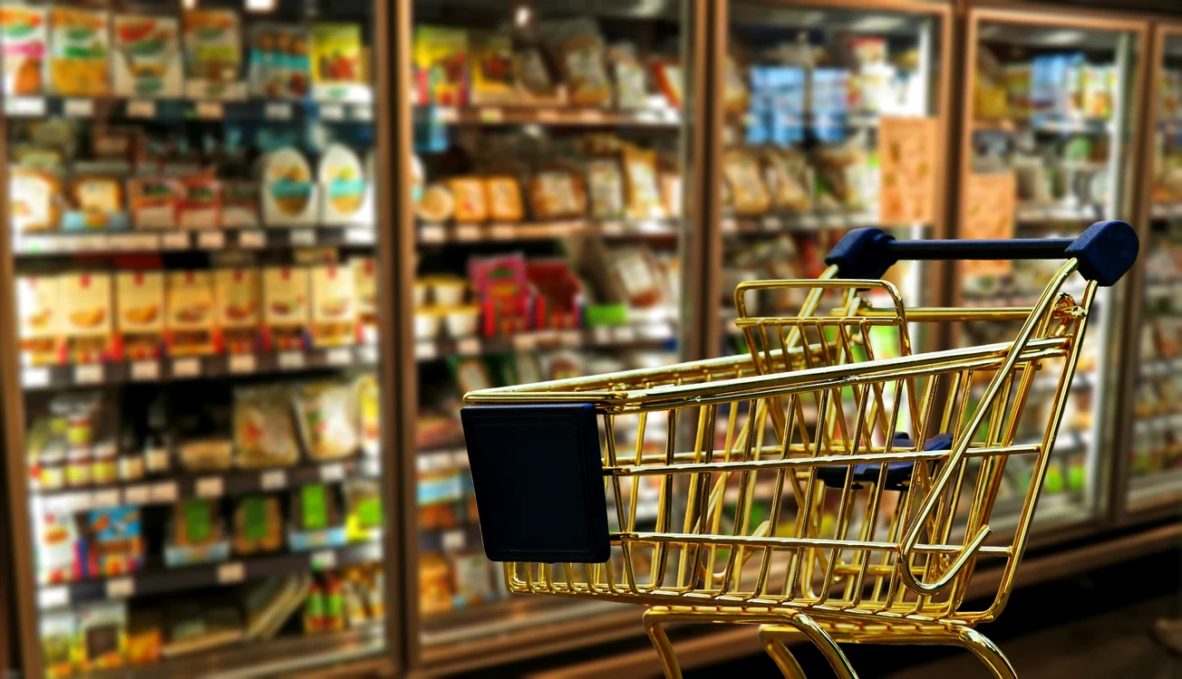 Coș de cumpărături gol, în fața rafturilor cu produse alimentare dintr-un supermarket