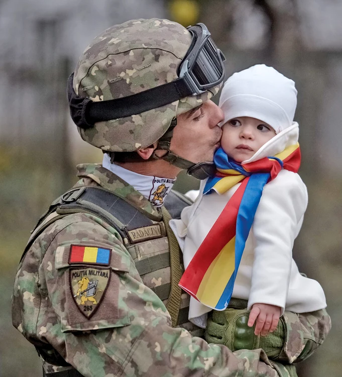 Tânărul polițist militar  își sărută cu foc copilașul, chiar înainte să intre în  formație pentru defilare 