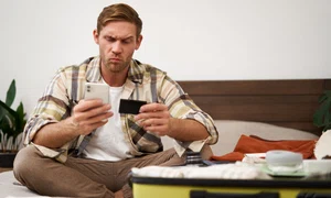 portrait man with thoughtful face sitting bed with suitcase paying online with credit card jpg