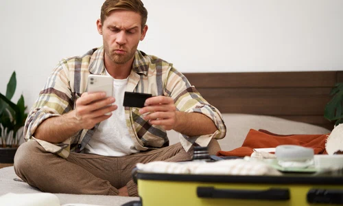 portrait man with thoughtful face sitting bed with suitcase paying online with credit card jpg