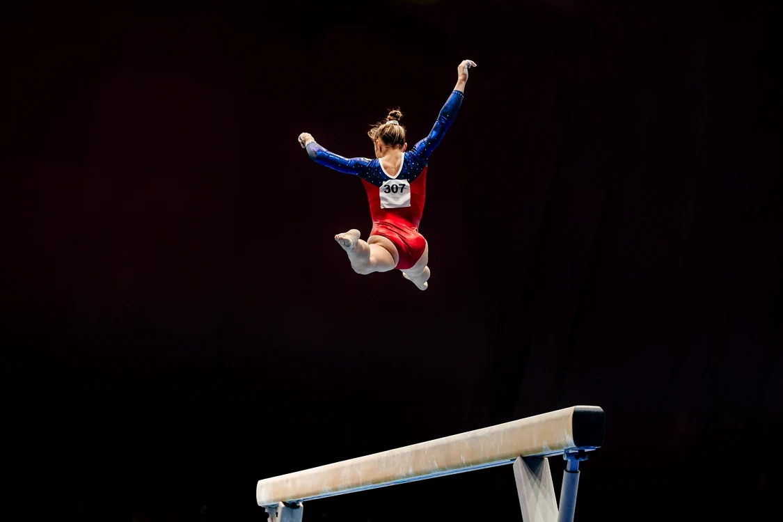 Gimnastă sărind în aer la bârnă. Shutterstock