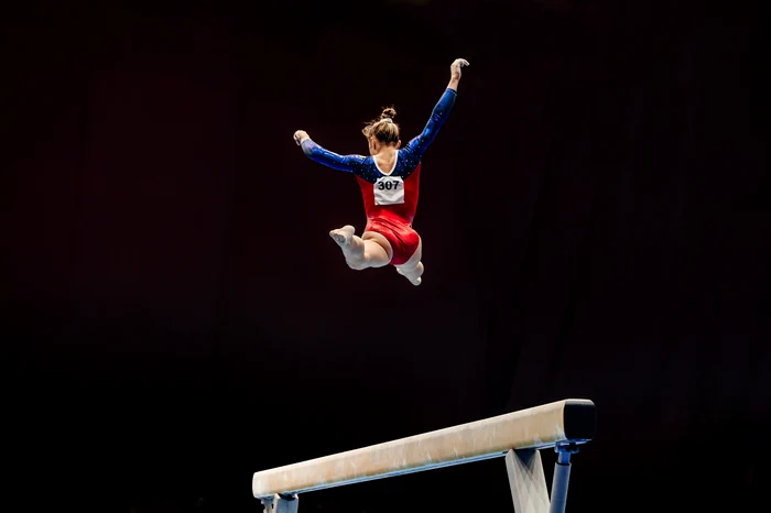 Gimnastă sărind în aer la bârnă. Shutterstock