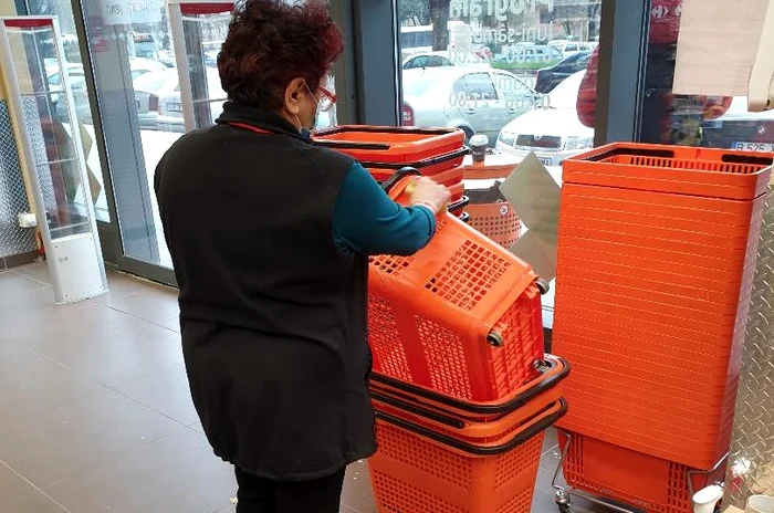 Femeia, angatata unui supermarket din București, folosește pentru dezinfectarea coșurilor detergent lichid, un burete și o lavetă