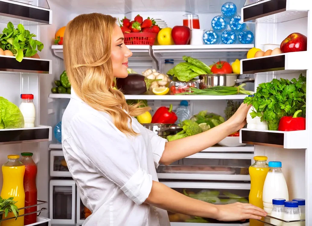Femeie care ia sau pune produse într-un frigider plin cu bunătăți proaspete și naturale Foto BobVila