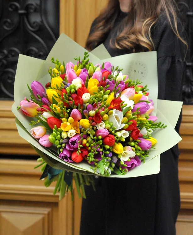 O femeie ține în brațe un imens buchet de flori de primăvară
