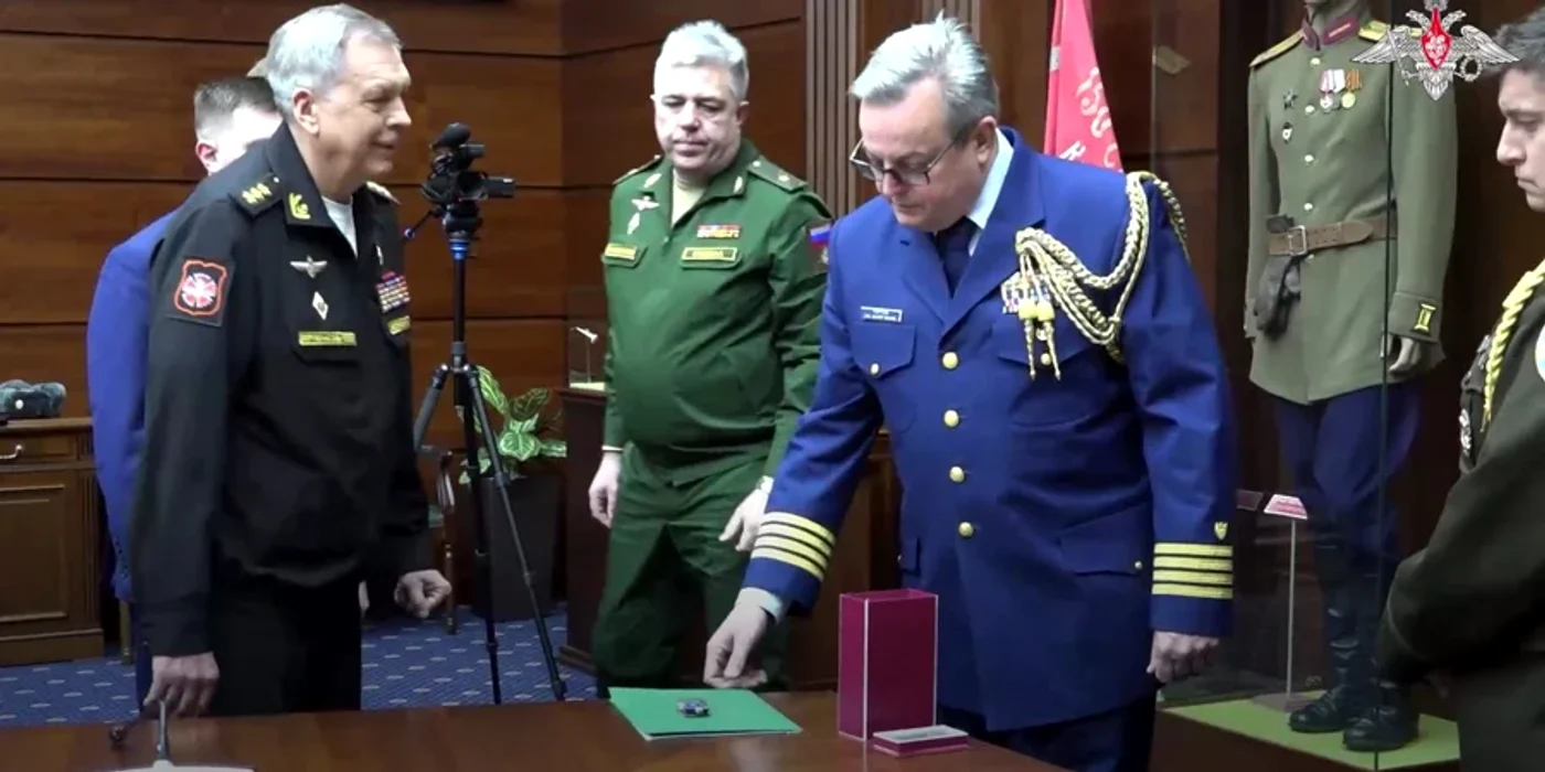 Amiralul Igor Kostîukov (dreapta), predând controlerul UAV-ului atașatului militar american