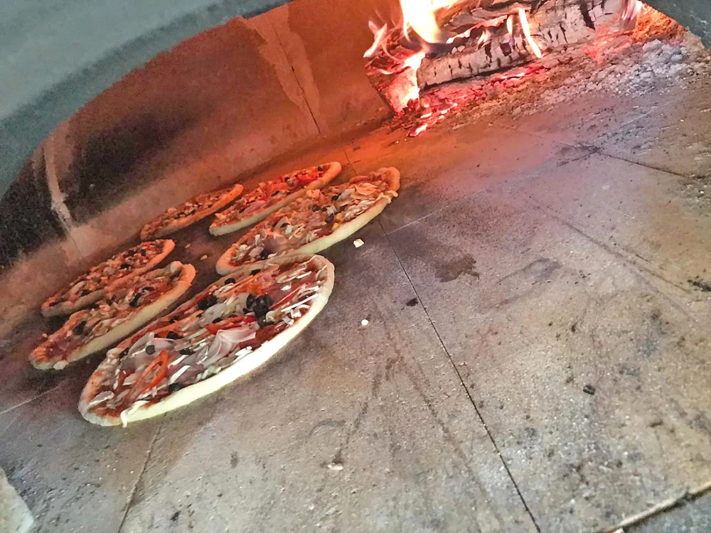 Pizza e gătită la  cuptorul cu lemne din  spatele autobuzului