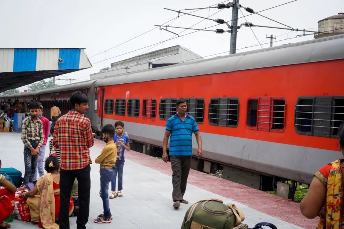 Pasageri pe un peron într-o gară din India, cu un tren garat